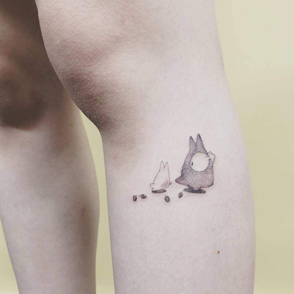 A charming minimalist Totoro tattoo with a small Totoro character and his companion, following a trail of tiny seeds – perfect for subtle yet adorable Ghibli fans