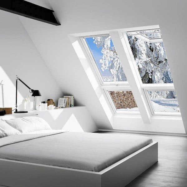 Bright attic bedroom with a sloped ceiling, modern decor, and snowy landscapes visible through large skylights