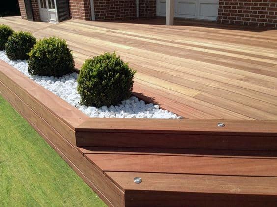 Wooden deck with built-in planter boxes, white stones, and neatly trimmed shrubs.