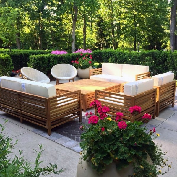 Brick seating area with wooden furniture and vibrant pink flowers, surrounded by lush greenery