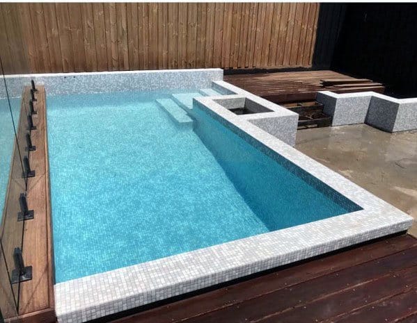 Compact backyard pool with light mosaic tiles, wooden accents, and modern design.
