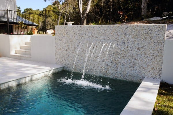 Modern backyard pool with a textured stone wall and cascading waterfall streams.