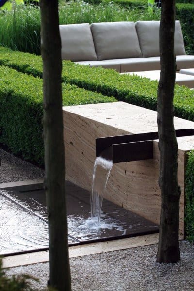 Modern backyard waterfall with a minimalist stone design and boxwood hedges.