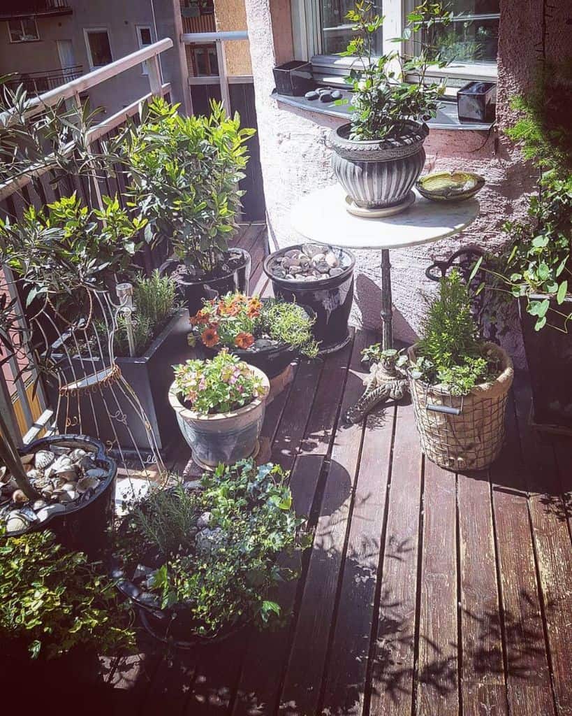 Small balcony with potted plants, flowers, and a round table creating a cozy garden space.
