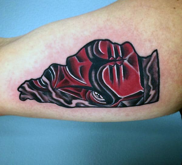 Tattoo of a stylized red and black face on an upper arm