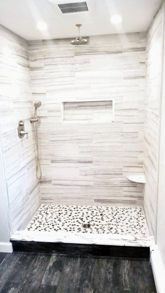 White shower with horizontal stone-like tiles and a pebble tile floor featuring a built-in shower niche.