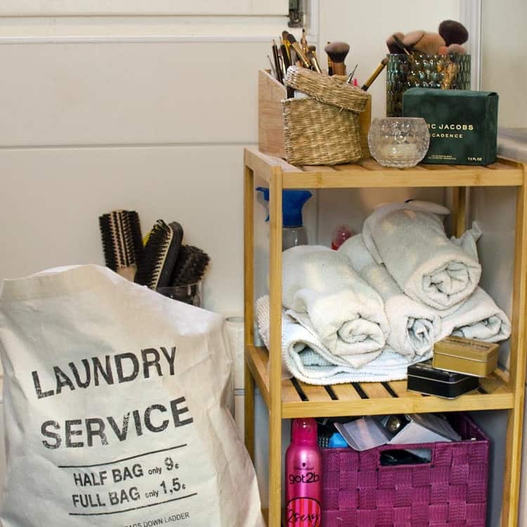 Small bathroom storage unit with rolled towels, makeup brushes, and laundry bag.