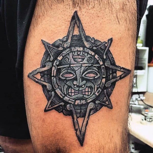 Aztec-inspired sun tattoo with a face at center on a thigh