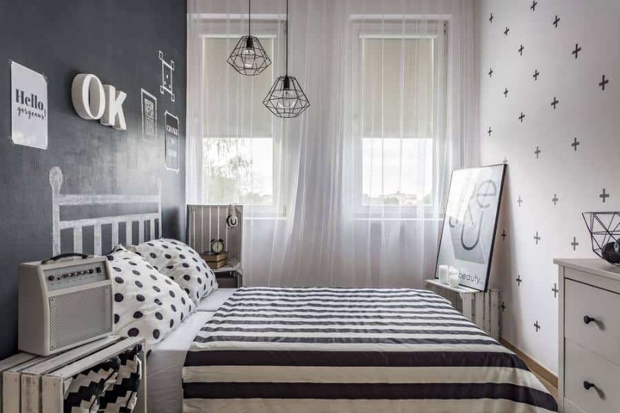 Modern bedroom with striped bedding, chalkboard accent wall, and geometric pendant lights.