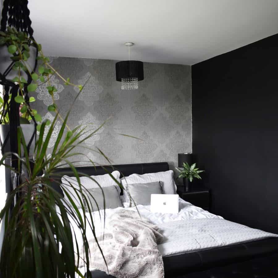 Modern bedroom with black and grey walls, cozy bedding, and hanging indoor plants.