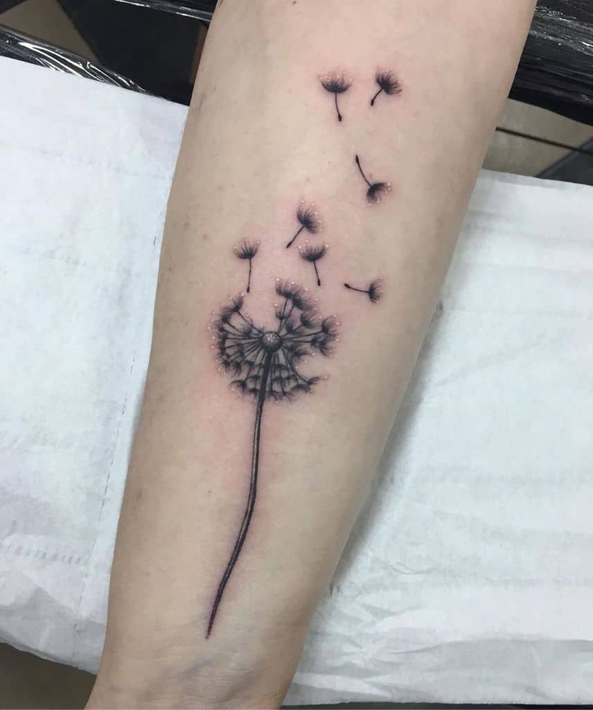 Realistic dandelion tattoo on the forearm with soft shading and seeds drifting away, symbolizing hope, change, and new beginnings.