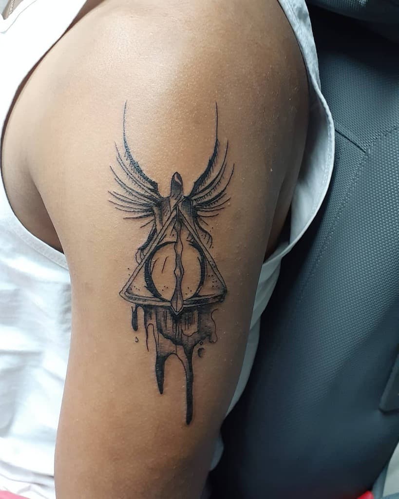Black ink Deathly Hallows tattoo on the upper arm featuring a hooded figure with wings, dripping ink effects, and intricate shading.