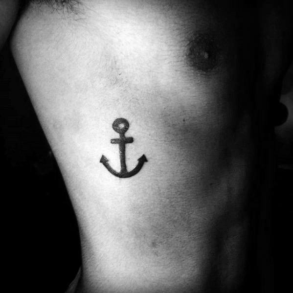 Small black anchor tattoo on the ribcage with a bold, simple design, symbolizing stability, strength, and a deep connection to the sea.