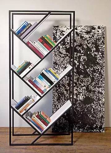 Modern slanted bookshelf with colorful books beside a black and white abstract painting