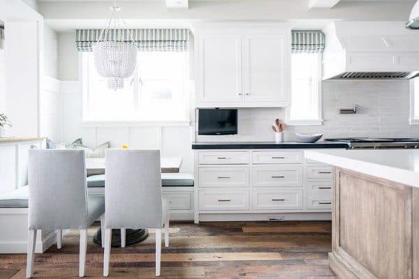 Bright kitchen nook with white cabinets, a small TV, a wooden island, and two gray chairs at a table