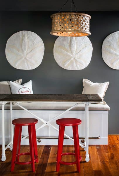 Modern dining nook with red stools, wooden table, and large white wall art under a woven pendant light