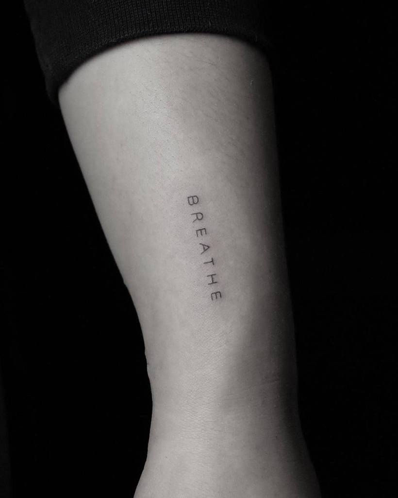 A minimalist tattoo of the word "BREATHE," elegantly aligned vertically on a person's forearm