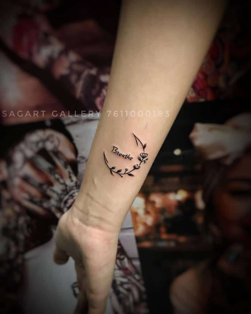 An elegant arm tattoo beautifully intertwines the word "Breathe" with delicate leaves and an intricate butterfly design