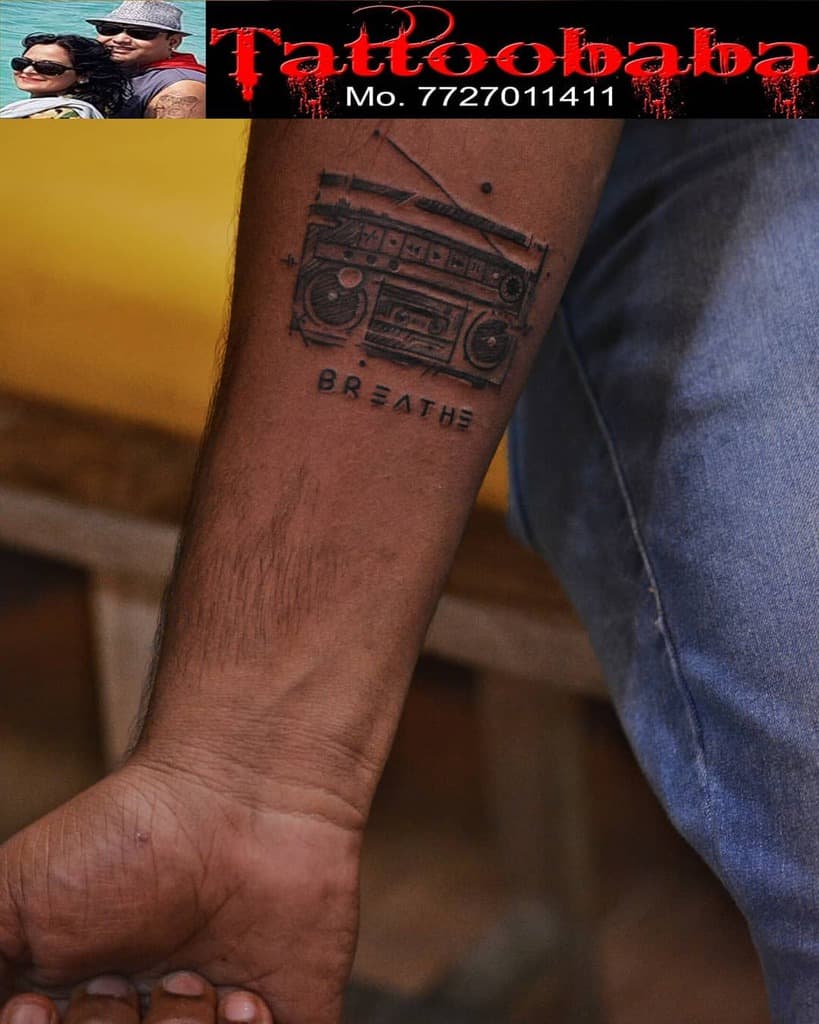 A forearm tattoo featuring a retro boombox, perfectly paired with the calming word "Breathe" gracefully inked beneath it