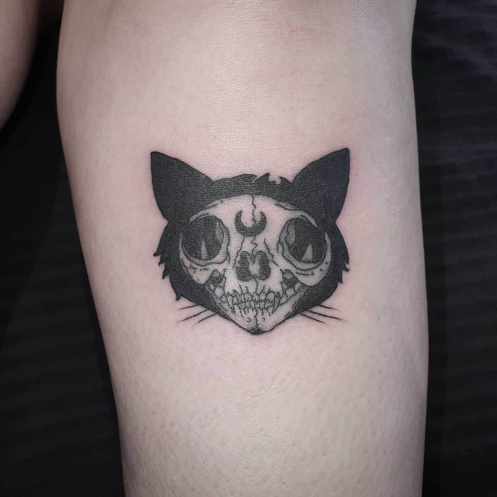 A tattoo featuring a cat skull adorned with a crescent moon on its forehead and large, black ears