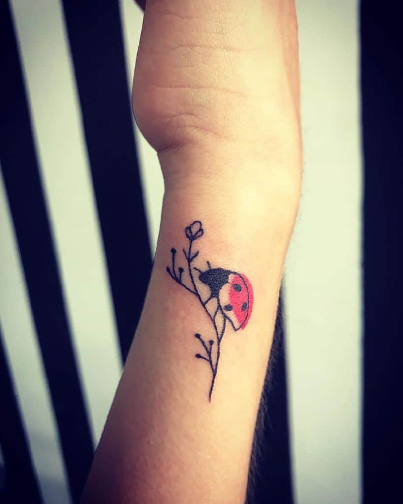 Minimalist ladybug tattoo on a delicate branch, featuring fine black lines and a soft red touch for an elegant and subtle wrist design.
