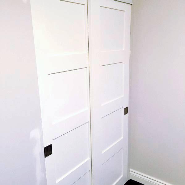 White sliding closet doors with black handles in a light gray room offer sleek storage solutions