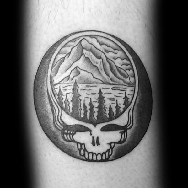 Black and grey Grateful Dead Steal Your Face skull tattoo featuring a mountain, lake, and forest scene inside the skull dome.