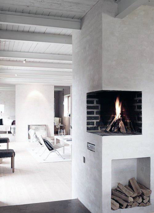 Minimalist corner fireplace with black brick interior, white walls, and built-in wood storage.