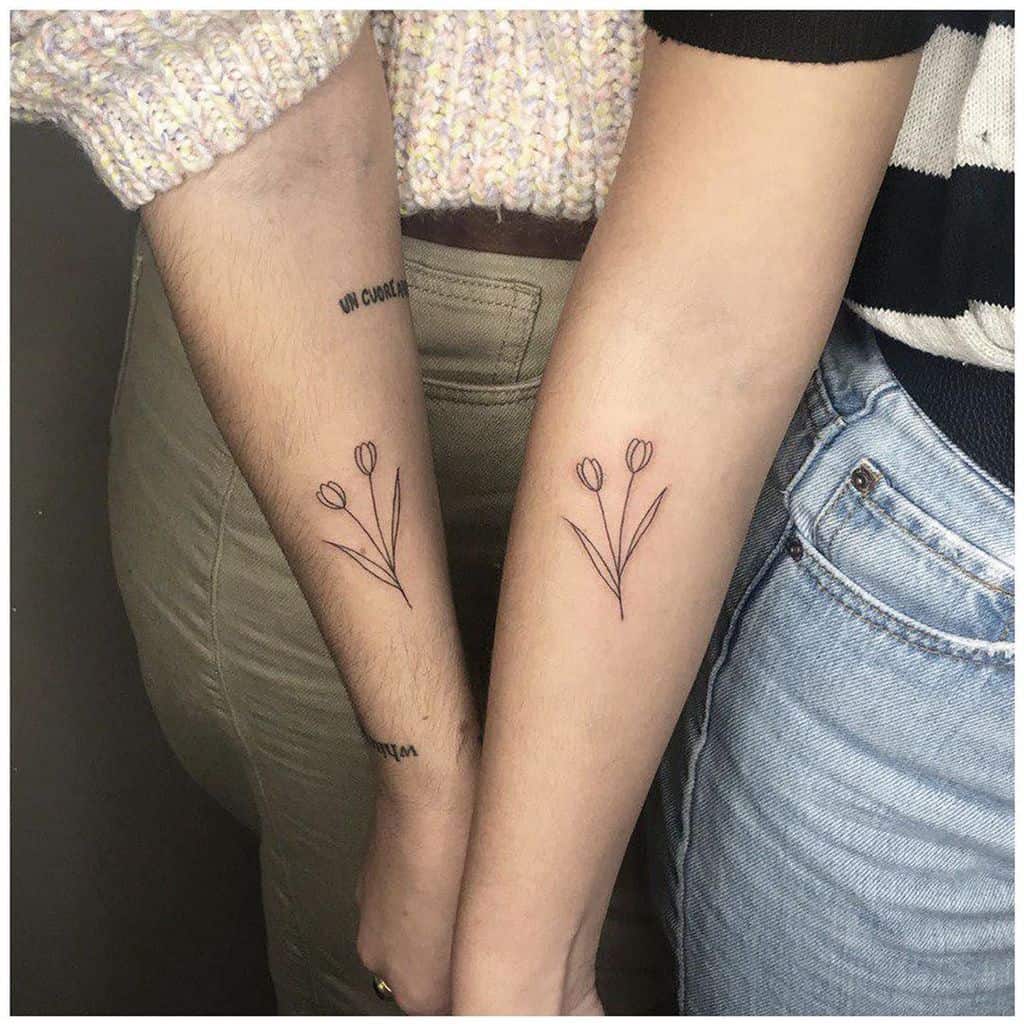 Matching minimalist tulip tattoos on two forearms, featuring two delicate flowers with thin stems and simple line work.