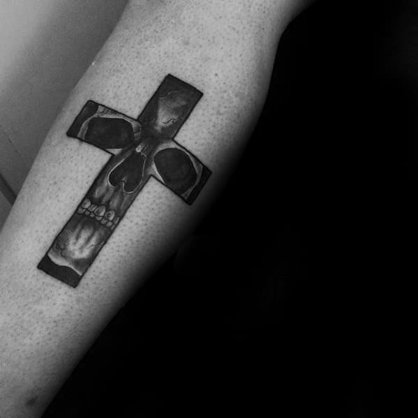 Tattoo of a cross with a skull in the center on a person's forearm