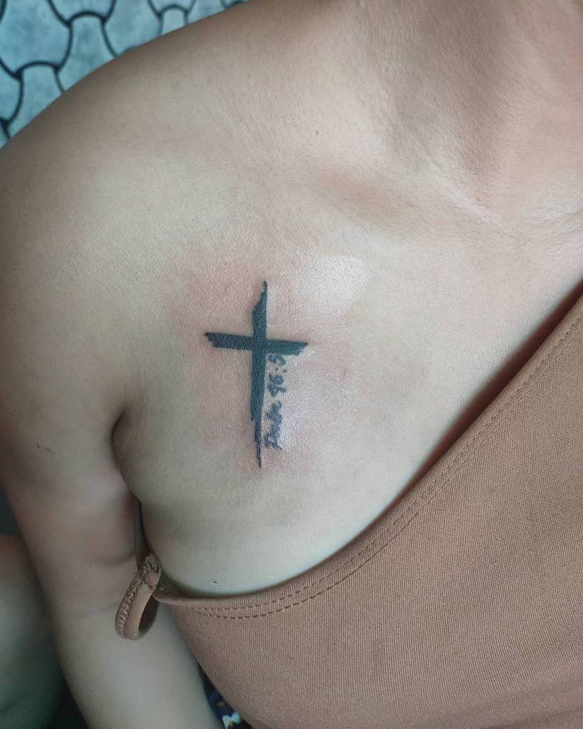A striking black cross tattoo graces the upper chest, near the shoulder