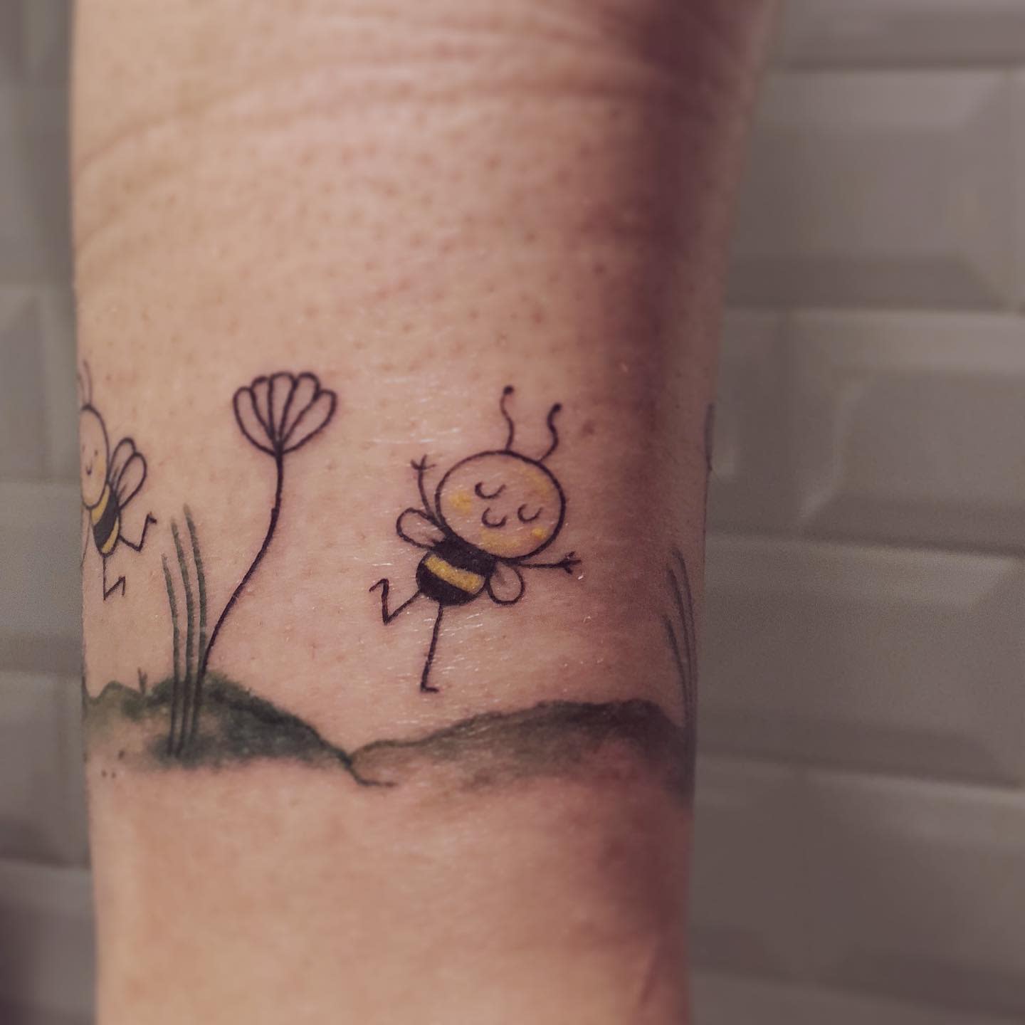 Adorable tattoo of happy dancing bees with tiny flowers and grass