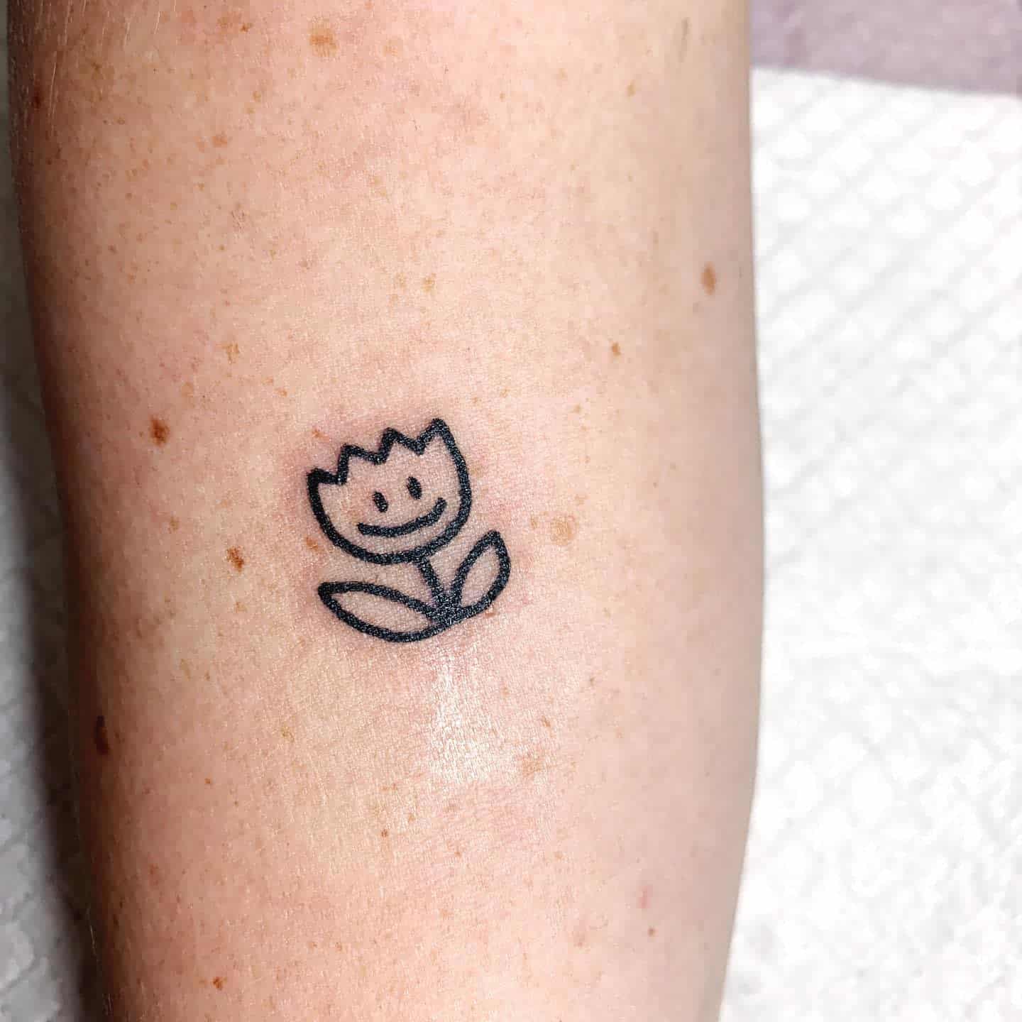 Minimalist smiling flower tattoo with simple black outlines