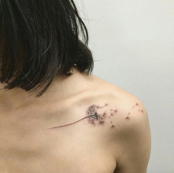 Delicate dandelion tattoo on the collarbone with seeds drifting away, symbolizing freedom, dreams, and new beginnings.
