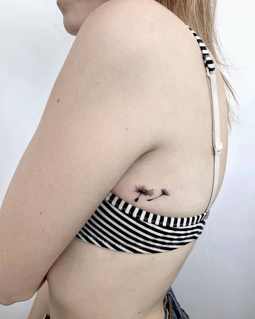 Minimalist dandelion seed tattoo on the ribcage, symbolizing lightness, freedom, and embracing life's journey.