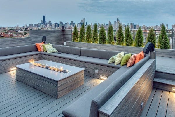 Rooftop deck with gray seating, colorful pillows, firepit table, and city skyline view.