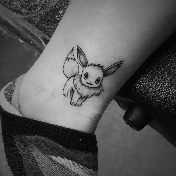 Detailed Eevee tattoo in black and gray shading, featuring a cheerful pose with large ears and fluffy fur details