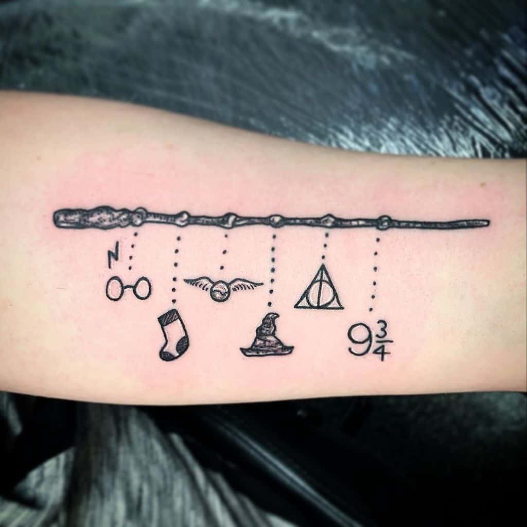 Minimalist Harry Potter tattoo featuring a wand with hanging charms, including glasses, a sock, the Golden Snitch, Deathly Hallows, Sorting Hat, and platform 9¾.