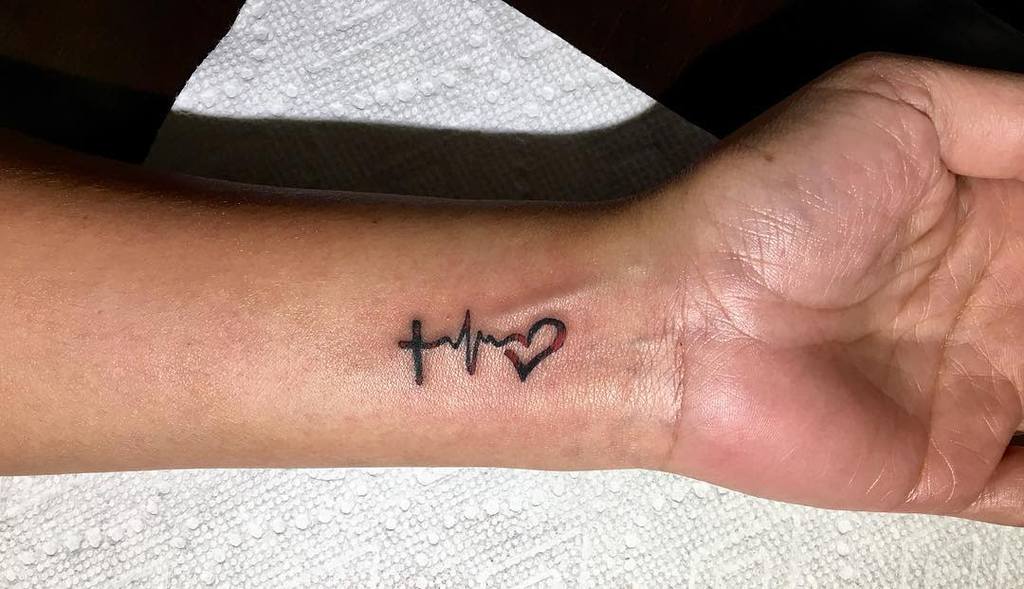 Small wrist tattoo of a cross, heart, and heartbeat line