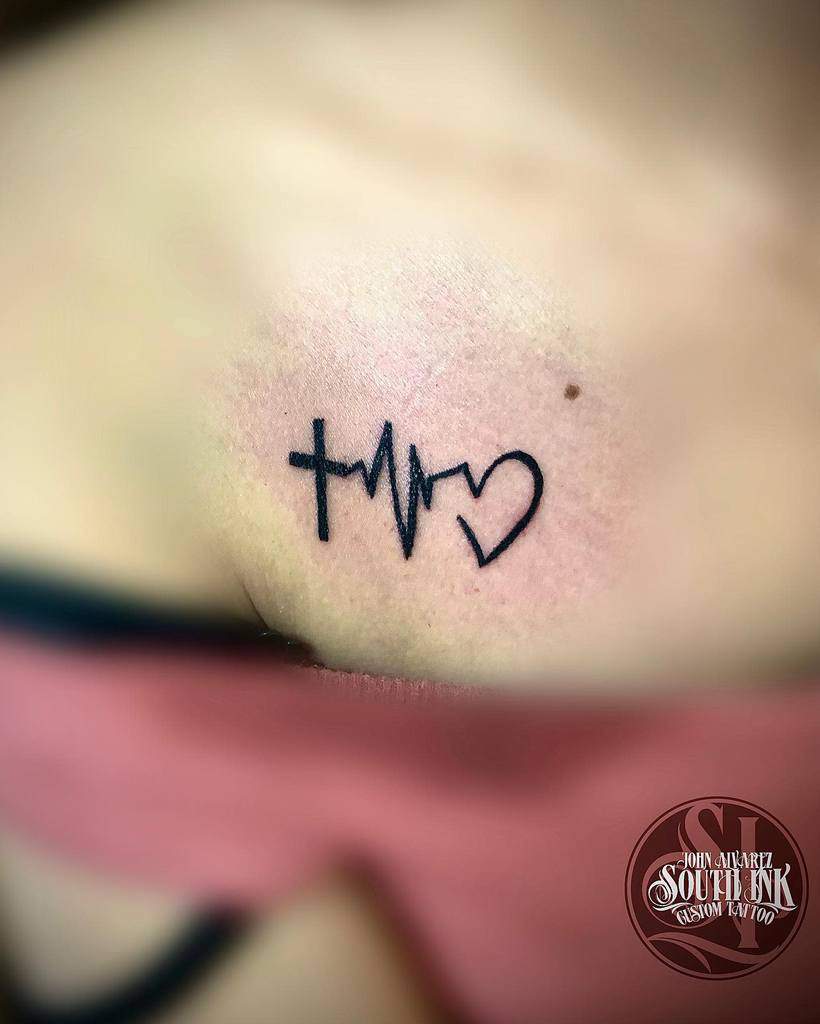 Small tattoo of a cross, heartbeat line, and heart design on a chest