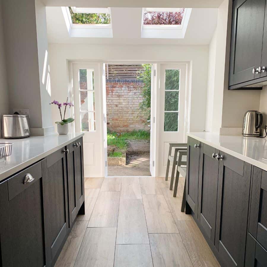 Compact galley kitchen with dark cabinets, bright skylights, and French doors opening to a garden.