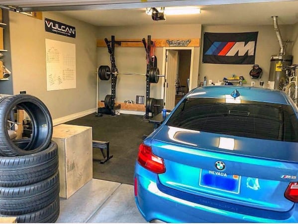 Garage gym with squat rack, weight plates, bench, and plyo box in a shared space with a parked car.