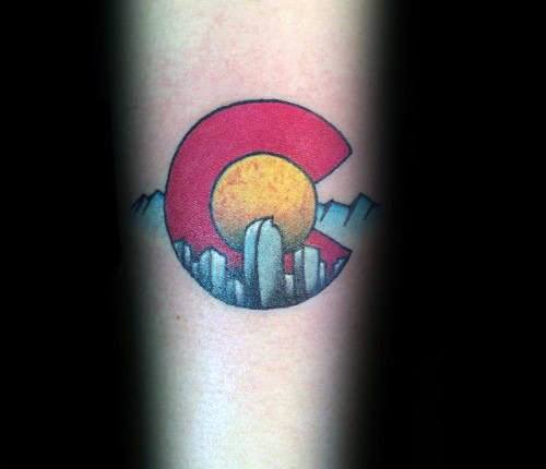 Small forearm tattoo of the Colorado flag “C” with Denver skyline and mountain peaks inside, featuring bold red, yellow, and blue tones.