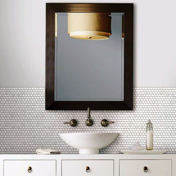 Bathroom with narrow mirror, white hexagon tile backsplash, vessel sink, and brass fixtures.