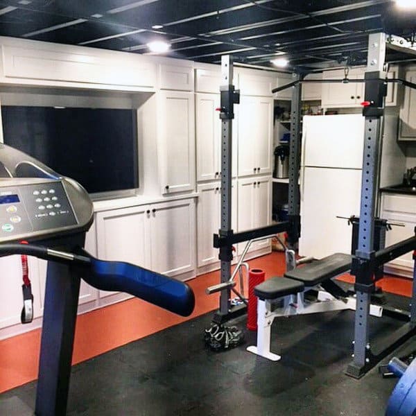 Home gym with treadmill, weight bench, and wall-mounted TV in a well-organized home space with white cabinets