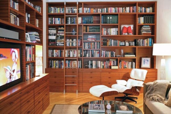 Cozy library with wooden shelves, a ladder, a white lounge chair, and a TV displaying an animated show