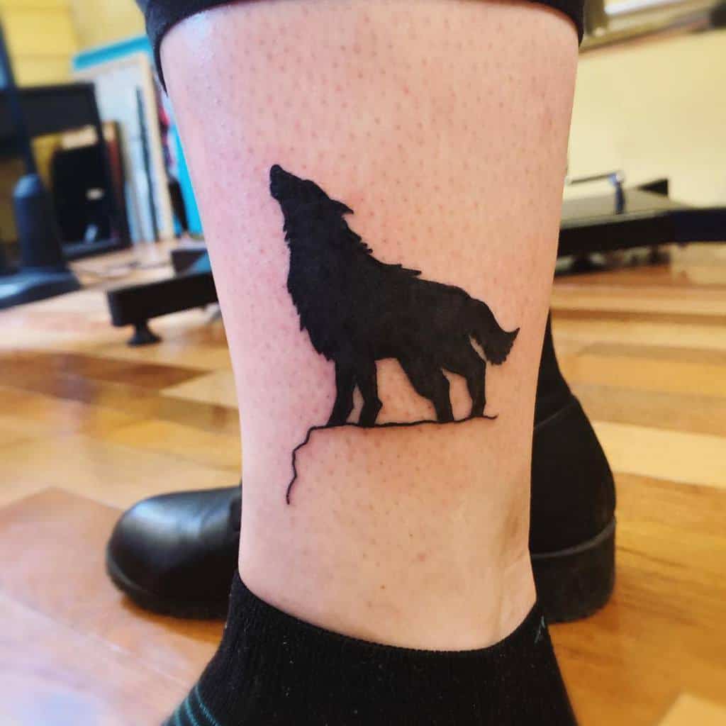 Silhouette tattoo of a howling wolf on a leg