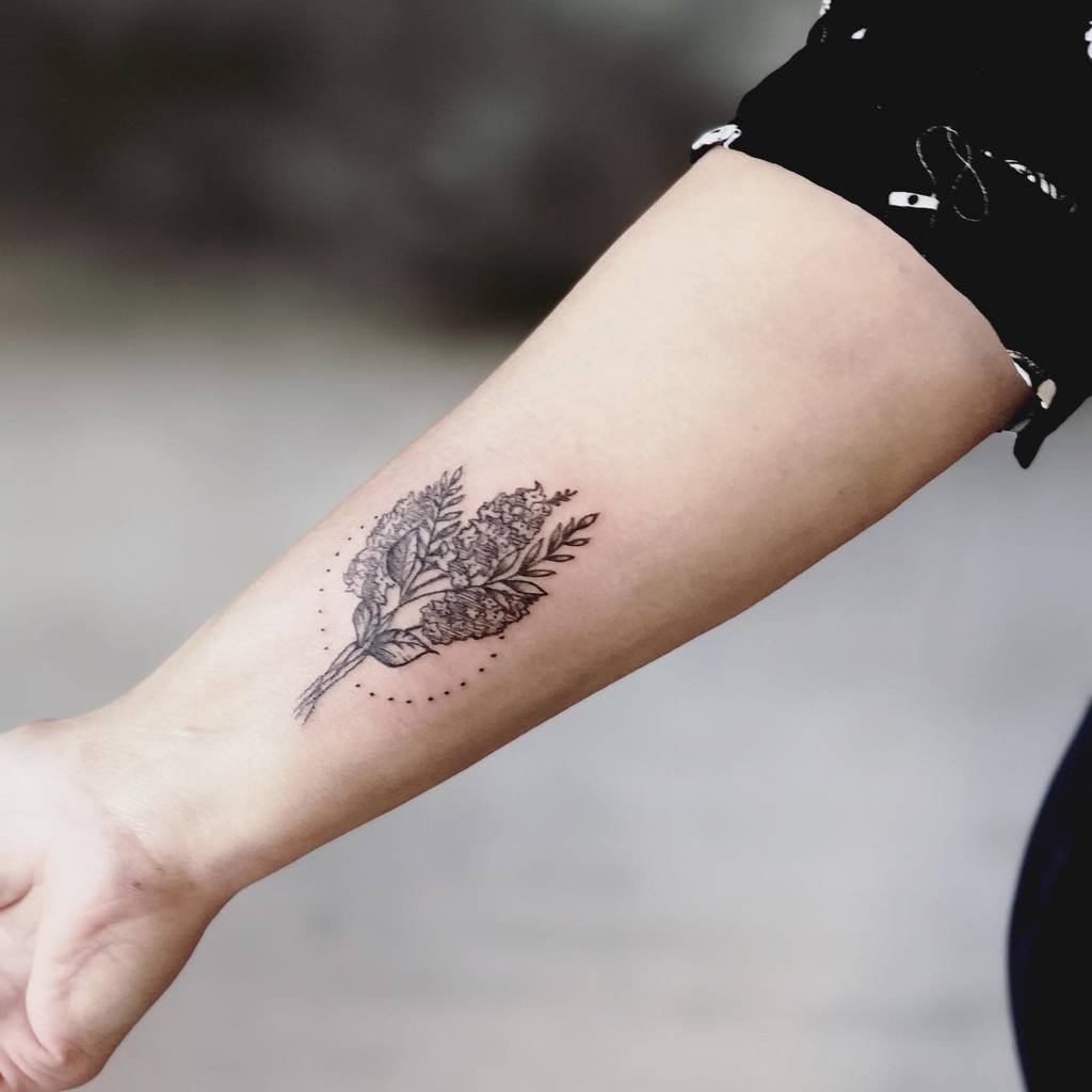 Black and grey forearm tattoo of a lilac bouquet with fine-line details, surrounded by subtle dotted ornamental accents.