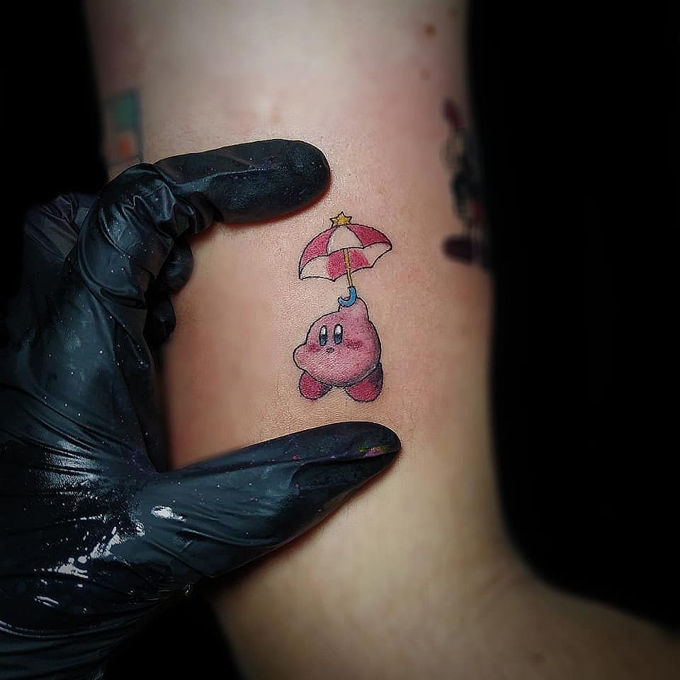 Tiny Kirby tattoo floating with a red-and-white parasol and star above of it, featuring soft shading and fine details