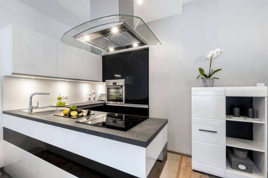Small modern kitchen with black countertops, white cabinets, and glass range hood.